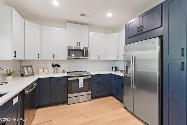 kitchen with backsplash, stainless steel appliances, white cabinets, and light wood-type flooring