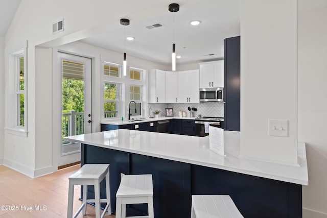 kitchen with appliances with stainless steel finishes, pendant lighting, white cabinets, a kitchen breakfast bar, and kitchen peninsula