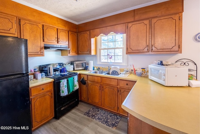 kitchen featuring brown cabinets, light countertops, under cabinet range hood, and black appliances