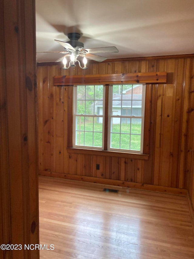 unfurnished room with ceiling fan, light hardwood / wood-style flooring, and wooden walls