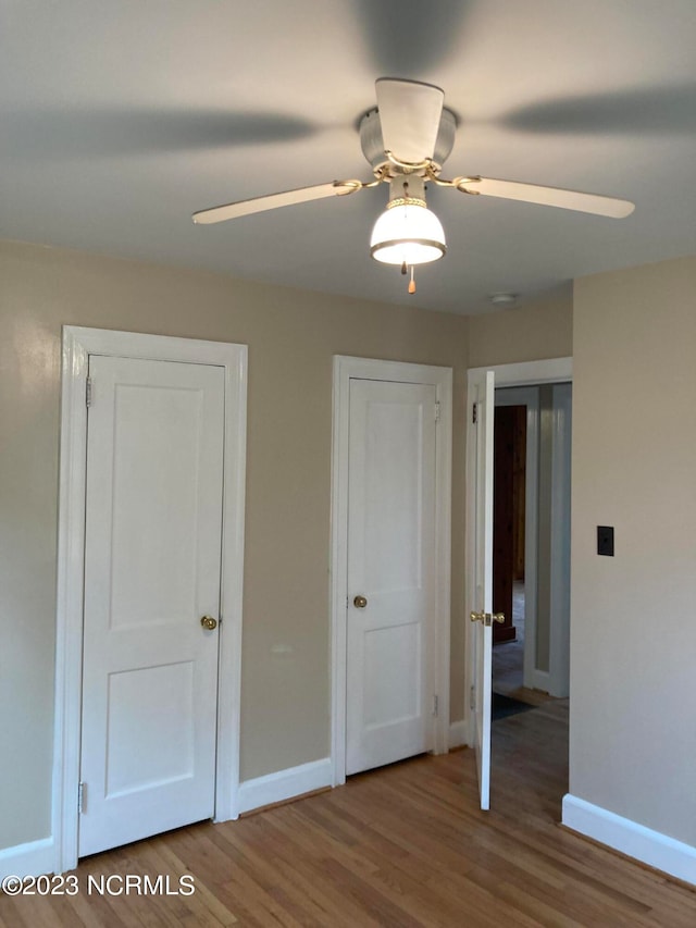 unfurnished bedroom with ceiling fan, two closets, and wood-type flooring