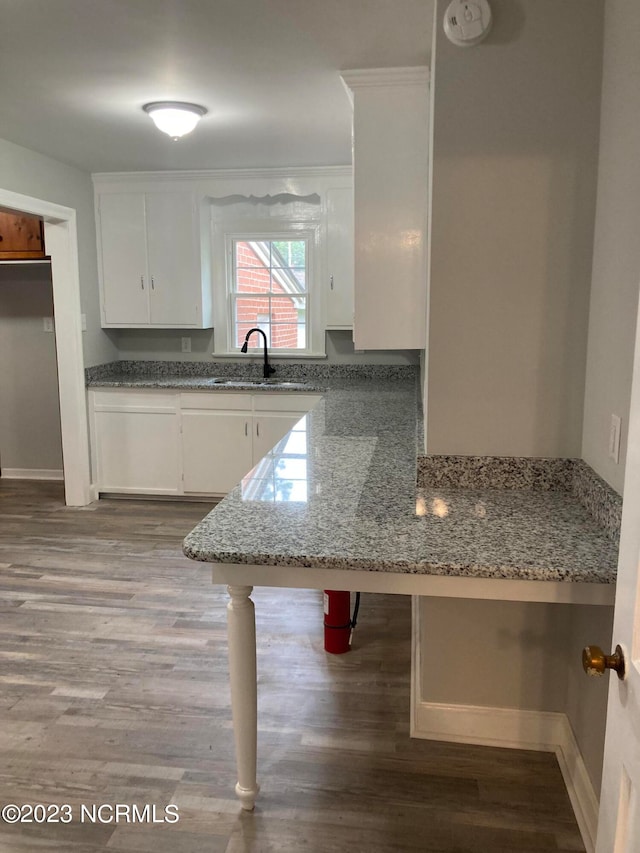 kitchen featuring stone counters, light wood-style floors, white cabinets, a sink, and a peninsula