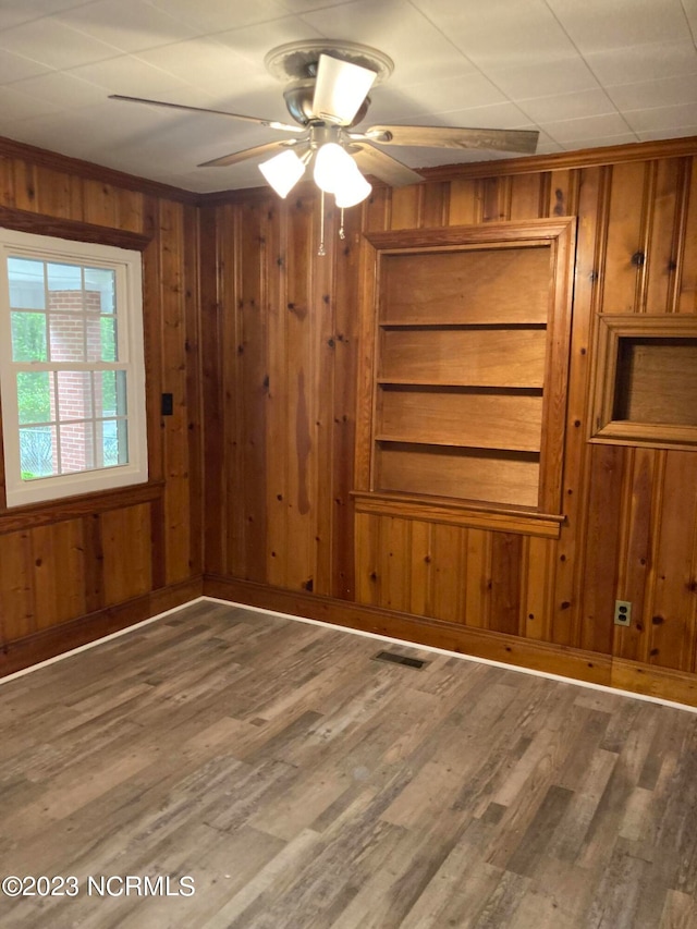 empty room featuring a ceiling fan, wood finished floors, visible vents, and wooden walls