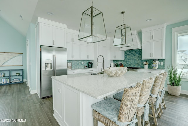 kitchen with backsplash, built in fridge, an island with sink, and wood-type flooring