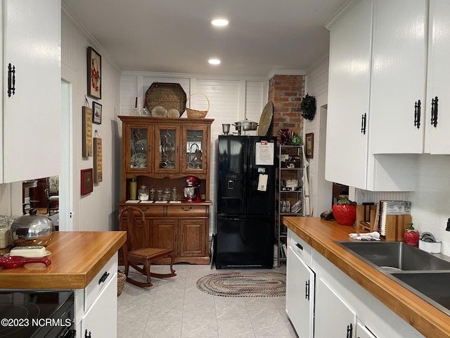 kitchen featuring brick wall, black refrigerator, light tile flooring, and white cabinetry