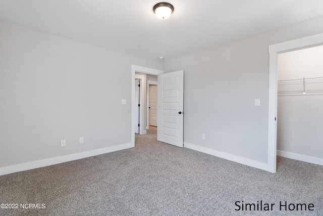 unfurnished bedroom featuring a closet, a walk in closet, and carpet