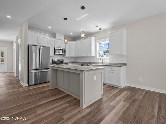 kitchen featuring white cabinetry, hanging light fixtures, a center island, stainless steel appliances, and light stone countertops