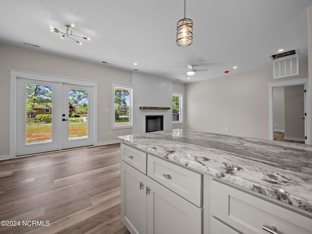 kitchen with pendant lighting, a wealth of natural light, light stone countertops, and white cabinets