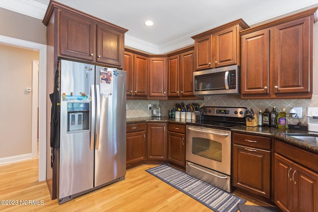 kitchen featuring backsplash, appliances with stainless steel finishes, light wood-type flooring, dark stone countertops, and crown molding