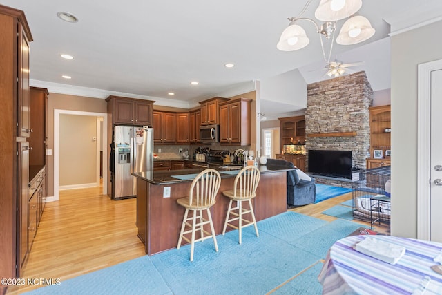 kitchen with appliances with stainless steel finishes, a fireplace, decorative light fixtures, ceiling fan with notable chandelier, and light wood-type flooring