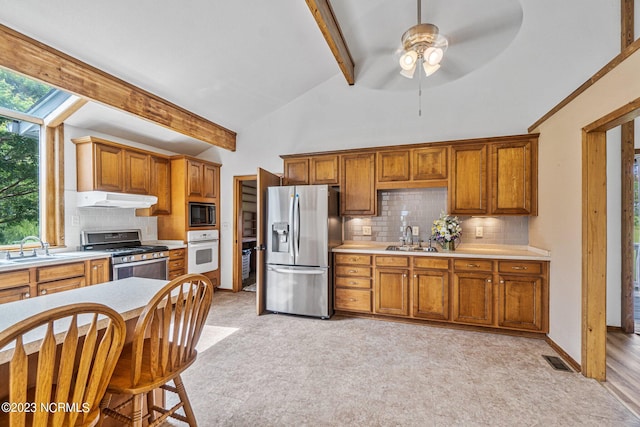 kitchen with ceiling fan, vaulted ceiling with beams, sink, stainless steel appliances, and decorative backsplash