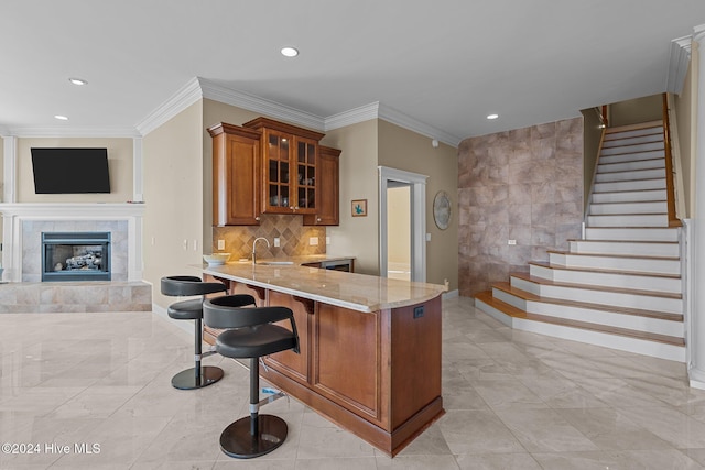 kitchen with a tile fireplace, sink, light stone counters, kitchen peninsula, and a breakfast bar area