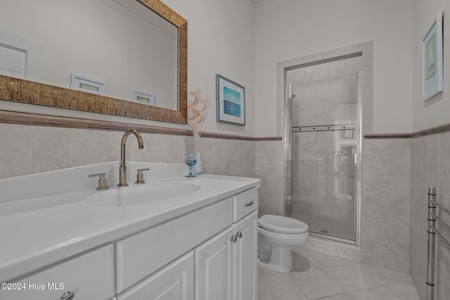 bathroom with tile patterned floors, toilet, a shower with door, vanity, and tile walls