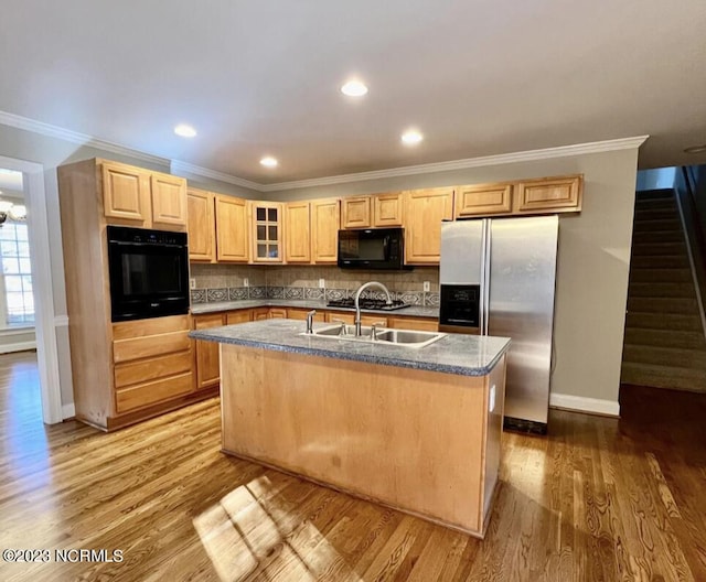 kitchen featuring light wood-type flooring, tasteful backsplash, crown molding, a center island with sink, and black appliances