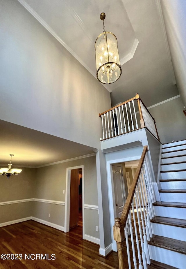 stairway with an inviting chandelier, crown molding, and dark wood-type flooring