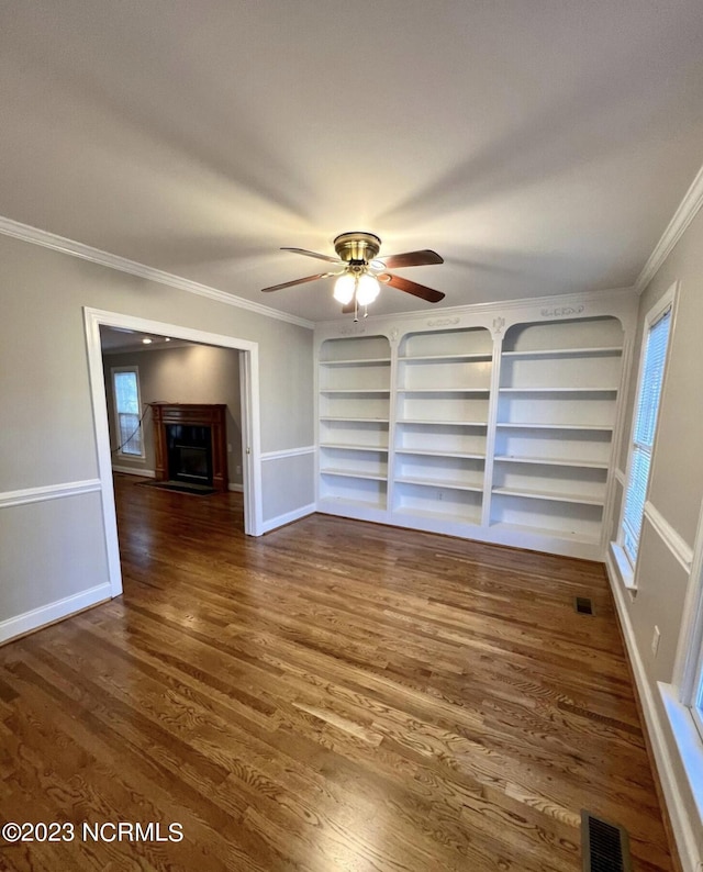 unfurnished living room with built in features, ornamental molding, ceiling fan, and dark wood-type flooring