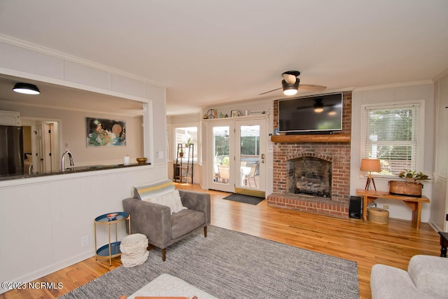 living room featuring light hardwood / wood-style flooring, a healthy amount of sunlight, a brick fireplace, and ceiling fan