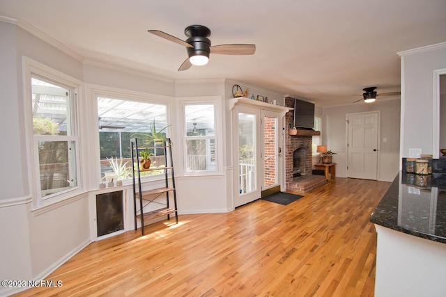 kitchen with light wood-type flooring, ceiling fan, a fireplace, dark stone countertops, and crown molding