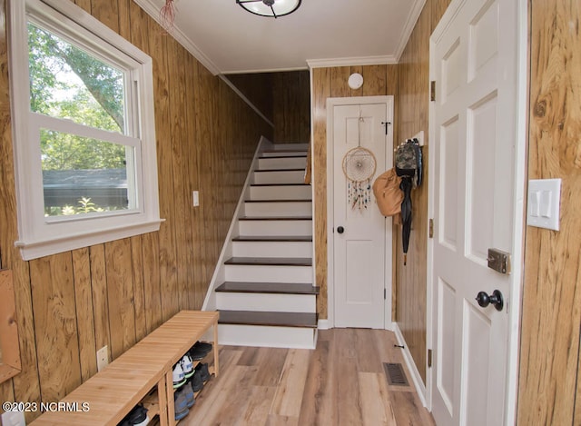 interior space with wood walls, ornamental molding, and light hardwood / wood-style floors