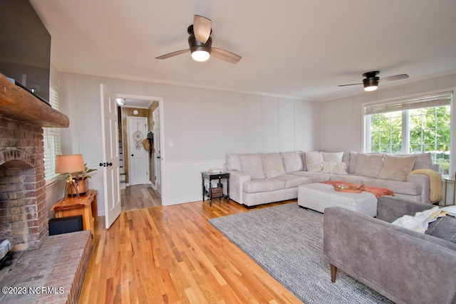 living room with light hardwood / wood-style flooring, ceiling fan, a brick fireplace, and crown molding