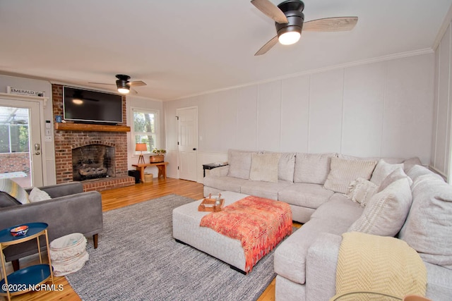 living room featuring ceiling fan, ornamental molding, a fireplace, and light hardwood / wood-style floors