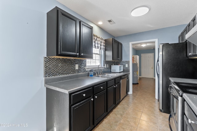 kitchen with sink, water heater, backsplash, light tile patterned flooring, and appliances with stainless steel finishes