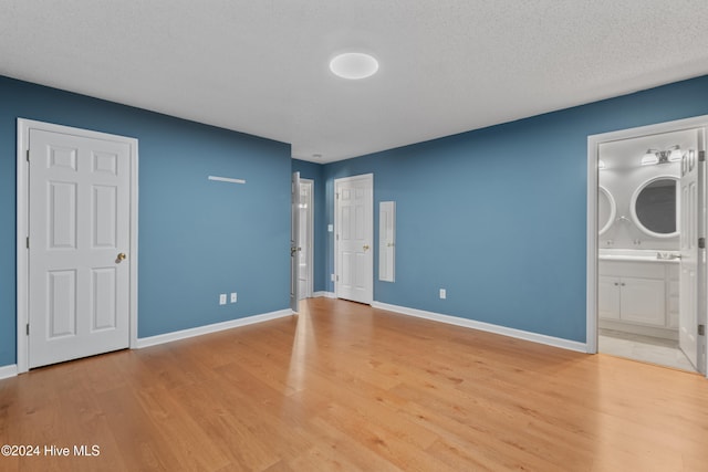 unfurnished bedroom featuring connected bathroom, light hardwood / wood-style flooring, and a textured ceiling