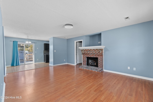 unfurnished living room with an inviting chandelier, light hardwood / wood-style floors, a textured ceiling, and a brick fireplace