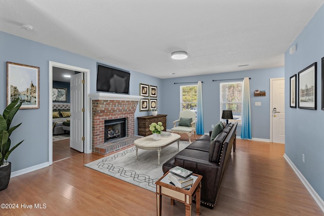 living room with wood-type flooring, a textured ceiling, and a brick fireplace