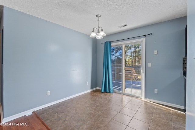 tiled empty room with a textured ceiling and a chandelier