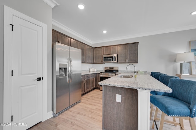 kitchen featuring appliances with stainless steel finishes, light hardwood / wood-style floors, sink, kitchen peninsula, and a breakfast bar