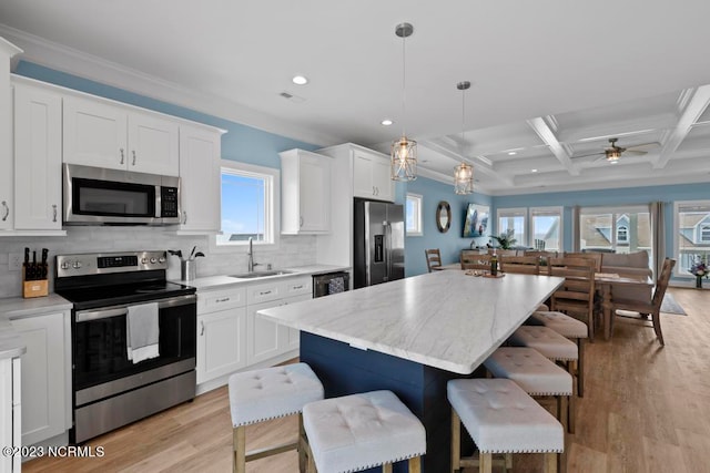 kitchen with appliances with stainless steel finishes, ceiling fan, a breakfast bar, coffered ceiling, and light hardwood / wood-style floors