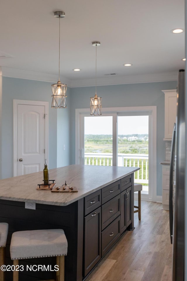 kitchen with pendant lighting, stainless steel refrigerator, a kitchen island, a breakfast bar area, and light hardwood / wood-style floors