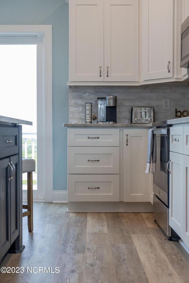 kitchen featuring backsplash, white cabinetry, light wood-type flooring, and stove