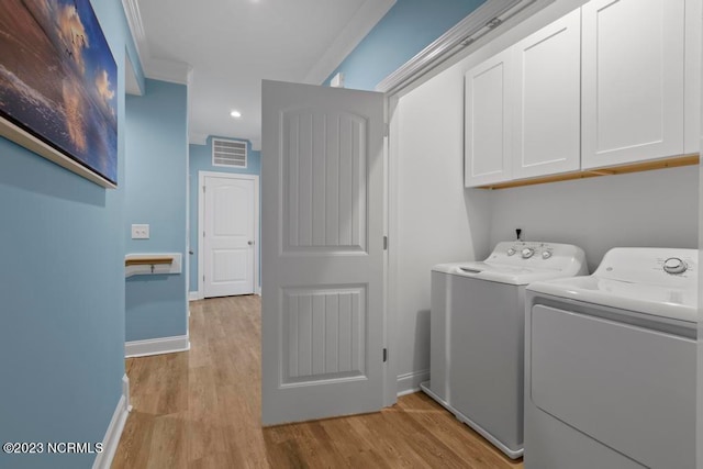 clothes washing area with crown molding, cabinets, light hardwood / wood-style floors, and washer and clothes dryer