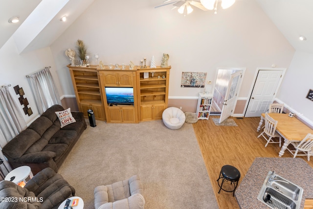 living room with a skylight, ceiling fan, light hardwood / wood-style flooring, and high vaulted ceiling