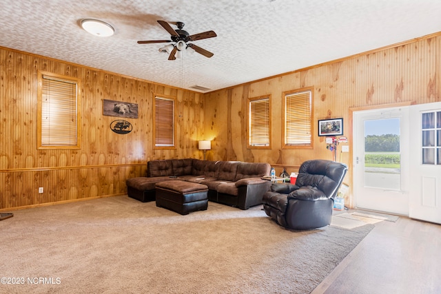 carpeted living room with a textured ceiling, ceiling fan, and wood walls