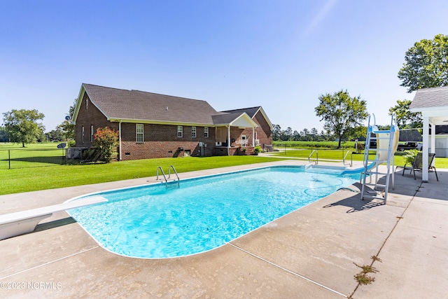 view of swimming pool with a lawn, a diving board, a patio area, and a water slide