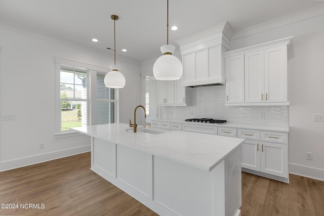 kitchen with hanging light fixtures, white cabinetry, sink, and a center island with sink