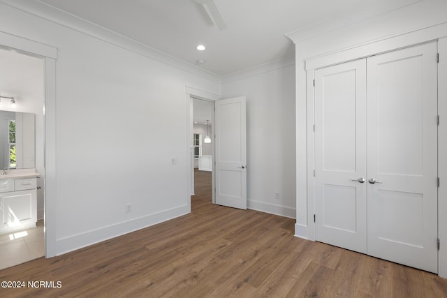 unfurnished bedroom with connected bathroom, crown molding, a closet, and hardwood / wood-style flooring