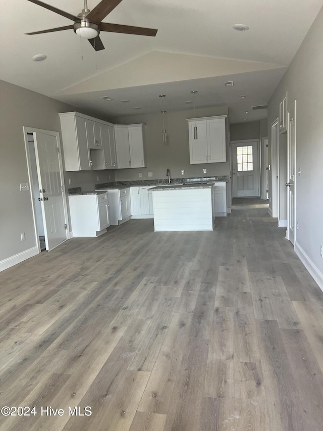 kitchen with vaulted ceiling, a kitchen island, sink, light hardwood / wood-style floors, and white cabinetry