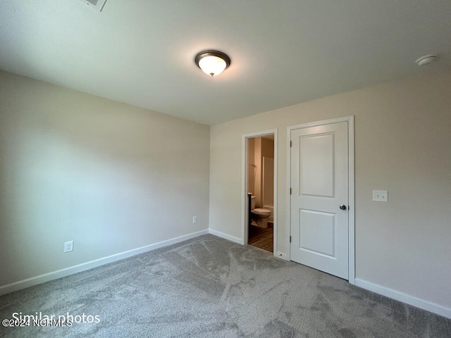 unfurnished bedroom featuring dark carpet and ensuite bath