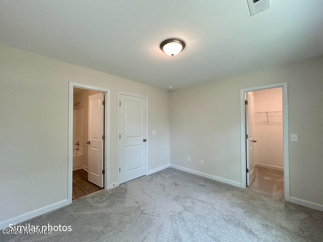 unfurnished bedroom featuring a spacious closet, light colored carpet, ensuite bathroom, and a closet