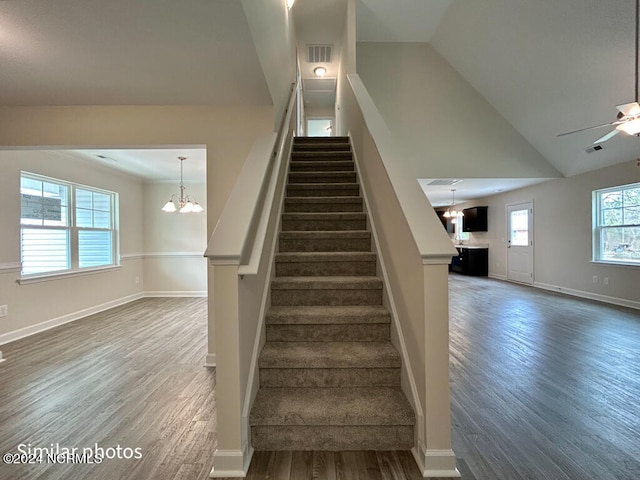 stairway with dark hardwood / wood-style flooring, high vaulted ceiling, ceiling fan with notable chandelier, and a healthy amount of sunlight