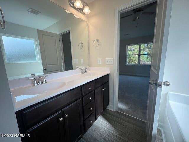 bathroom featuring dual sinks, oversized vanity, ceiling fan, wood-type flooring, and a bath