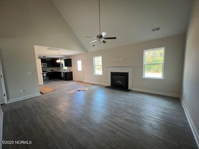 unfurnished living room with dark hardwood / wood-style flooring, plenty of natural light, high vaulted ceiling, and ceiling fan with notable chandelier