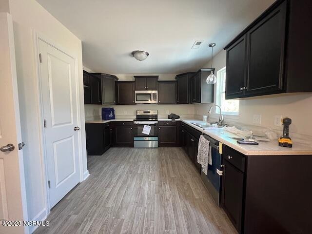 kitchen featuring light hardwood / wood-style flooring, stainless steel appliances, decorative light fixtures, and sink