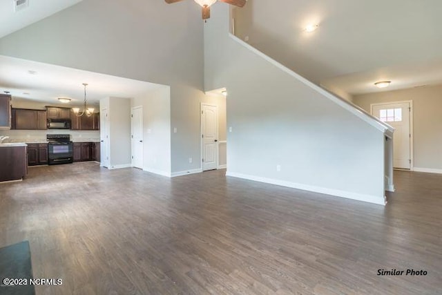 unfurnished living room with a towering ceiling, dark hardwood / wood-style floors, and ceiling fan with notable chandelier