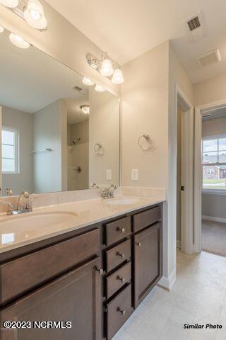 bathroom with oversized vanity, double sink, walk in shower, and tile flooring