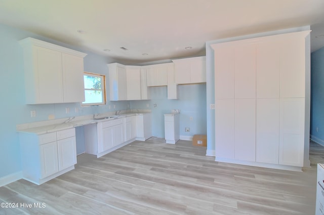 kitchen with white cabinets, light hardwood / wood-style flooring, sink, and light stone countertops